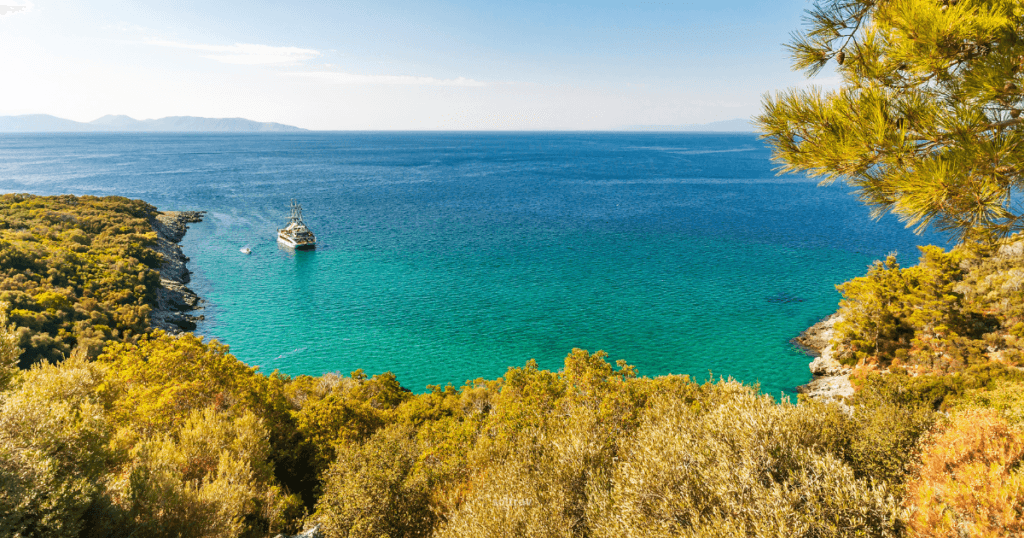 A picturesque view of Dilek National Park in Turkey, featuring a tranquil blue sea, a boat anchored near the shore, and lush greenery.