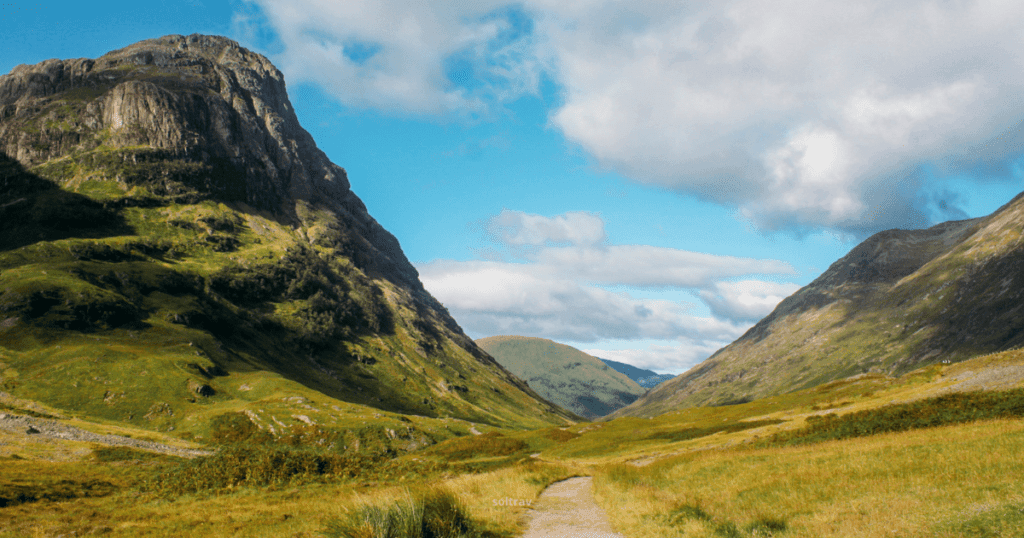 A serene view of Glencoe National Nature Reserve in Scotland, featuring a winding path through lush green valleys and towering mountains under a blue sky with scattered clouds.