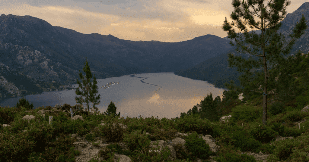 A scenic view of Peneda-Gerês National Park in Portugal, featuring a tranquil lake surrounded by mountains and lush vegetation at sunset.