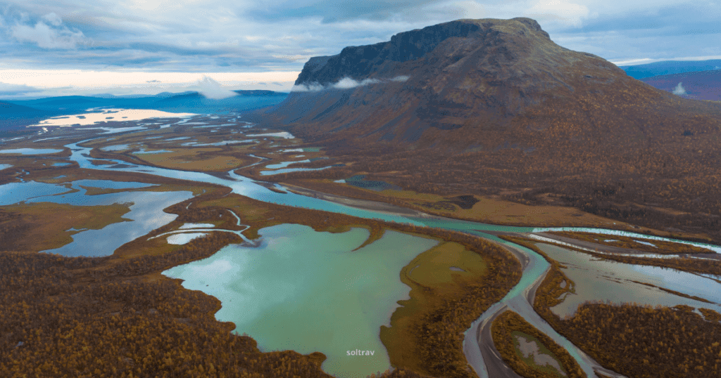 Aerial view of Sarek National Park in Sweden, showcasing winding rivers, glacial lakes, and rugged mountains under a cloudy sky.