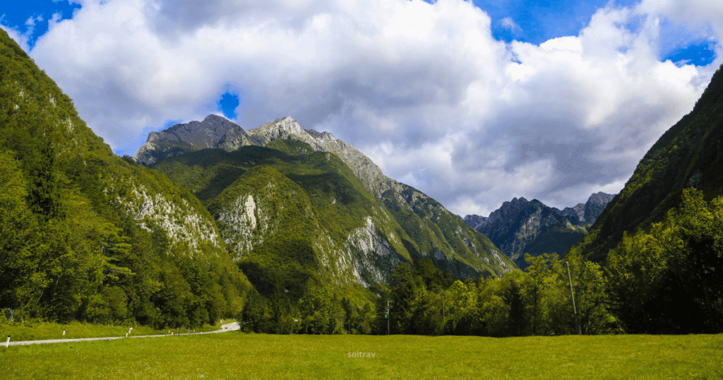 A panoramic view of Triglav National Park in Slovenia, showcasing lush green valleys, towering mountains, and a dramatic sky.