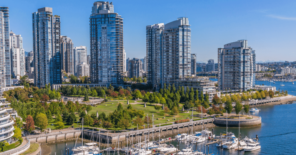 A scenic view of Vancouver, Canada, featuring modern high-rise buildings alongside a marina filled with boats. Lush green parks and trees are visible in the foreground, enhancing the urban landscape.