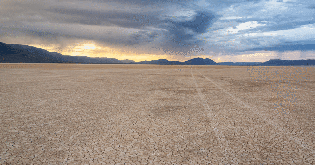 Expansive view of Alvord Desert in Oregon, featuring cracked earth and distant mountains under a dramatic sky.