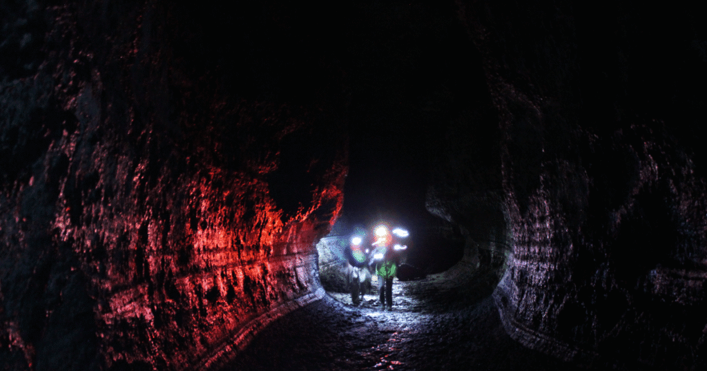 Explorers inside Ape Cave in Washington, illuminated by colorful headlamps against the dark, textured cave walls.