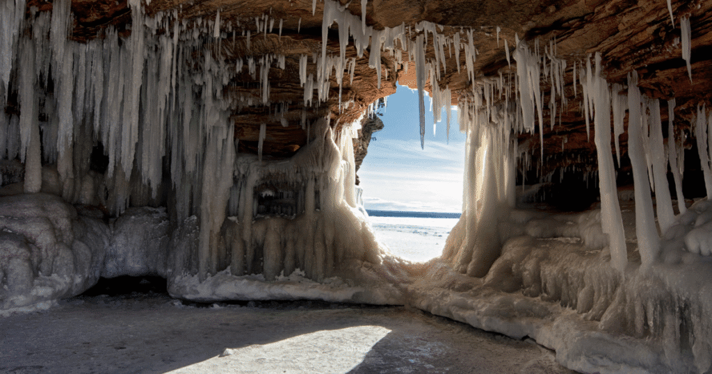 View from inside the Apostle Islands Ice Caves, featuring icicles hanging from the rocky entrance and a bright winter landscape beyond.