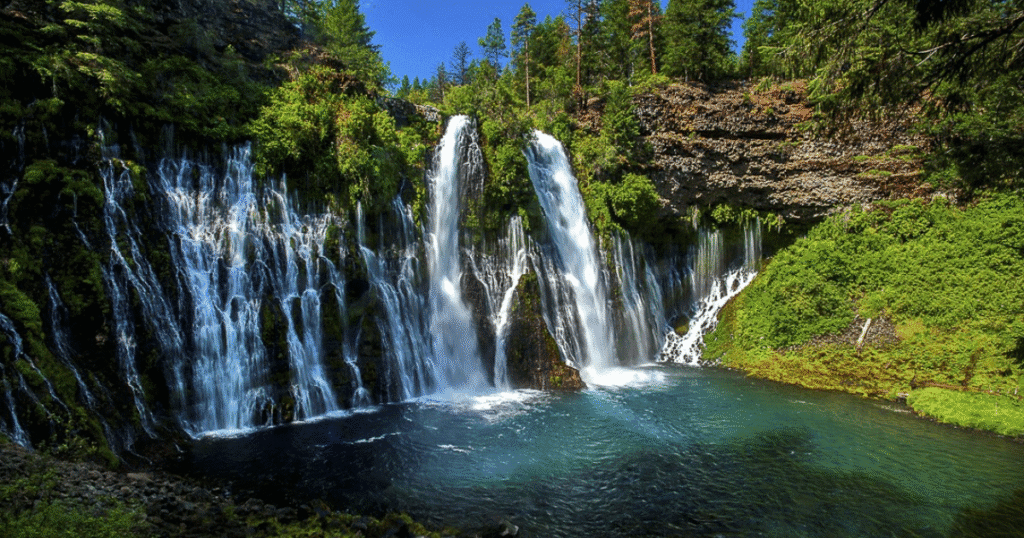 Breathtaking view of Burney Falls in California, featuring cascading waterfalls surrounded by lush greenery and a tranquil blue pool.