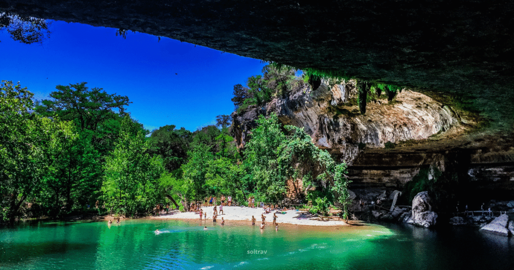 View of Hamilton Pool Preserve in Texas, featuring a natural swimming hole surrounded by lush greenery and people enjoying the water.