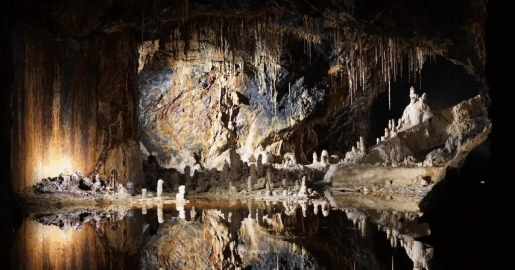 Interior view of Lava River Cave in Arizona, showcasing unique rock formations and a reflective pool under soft lighting.