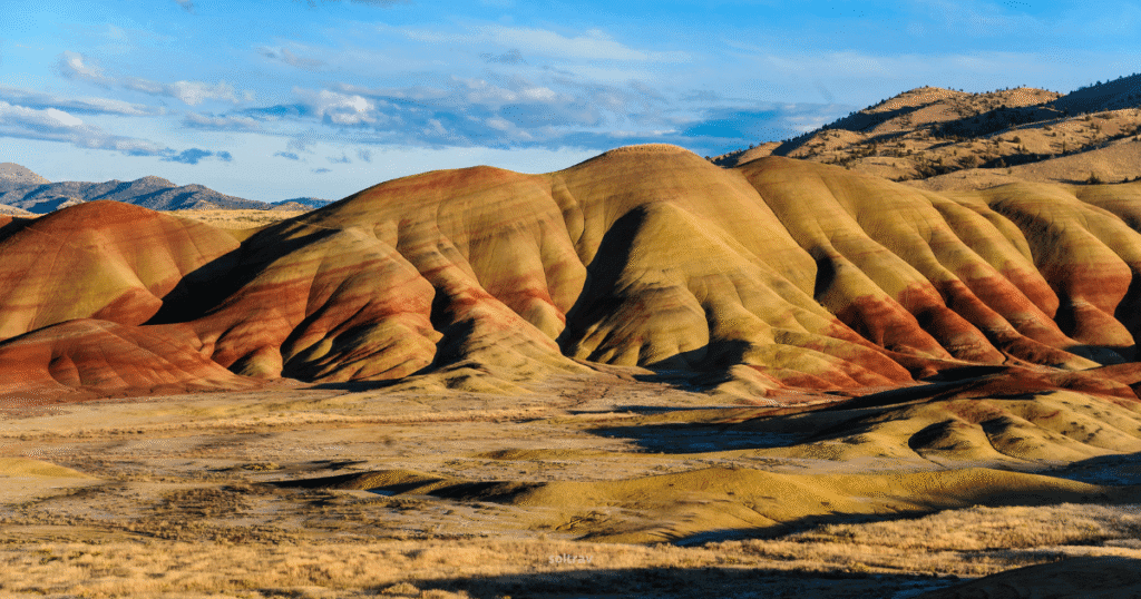 Vibrant landscape of Painted Hills in Oregon, showcasing rolling hills with striking red, yellow, and brown hues under a blue sky.