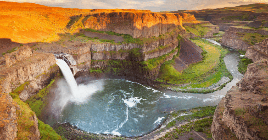 View of Palouse Falls in Washington, featuring a dramatic waterfall cascading into a circular pool surrounded by rugged cliffs and lush greenery.