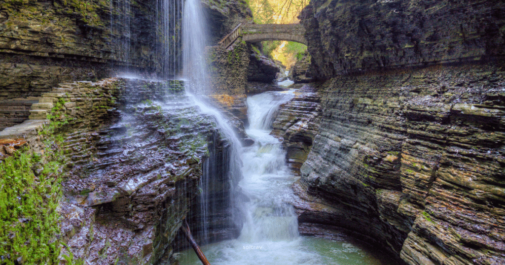 Waterfall cascading through the gorge at Watkins Glen State Park, with a stone bridge arching over the water.