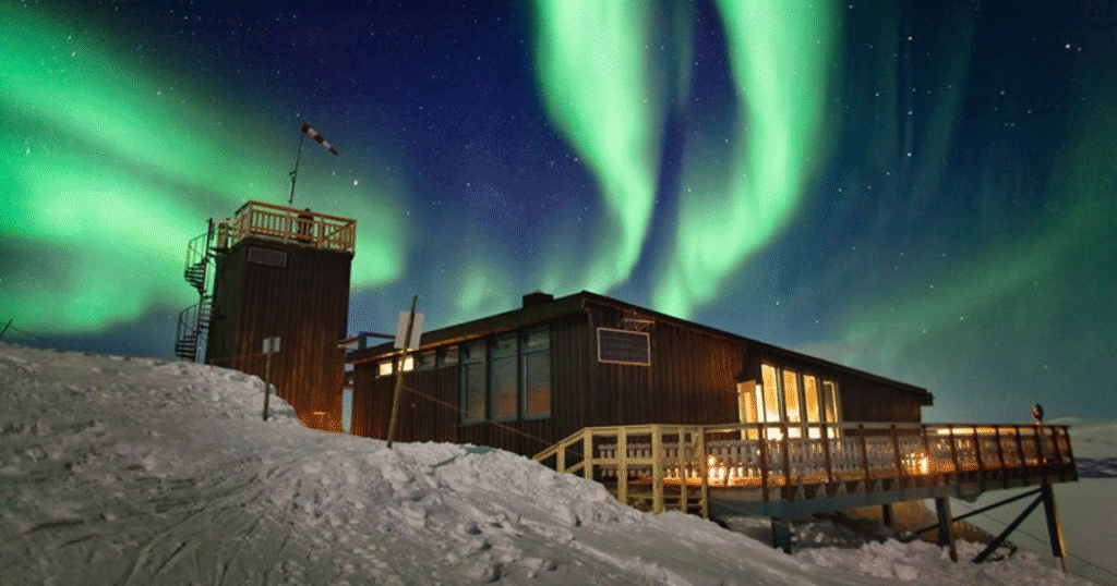 Abisko National Park lodge illuminated by the Northern Lights, with vibrant green auroras dancing in the night sky.