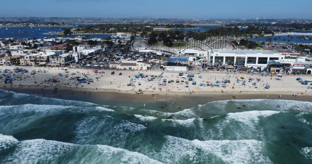 Aerial view of Belmont Park in California, featuring a beach, amusement park rides, and a bustling shoreline.