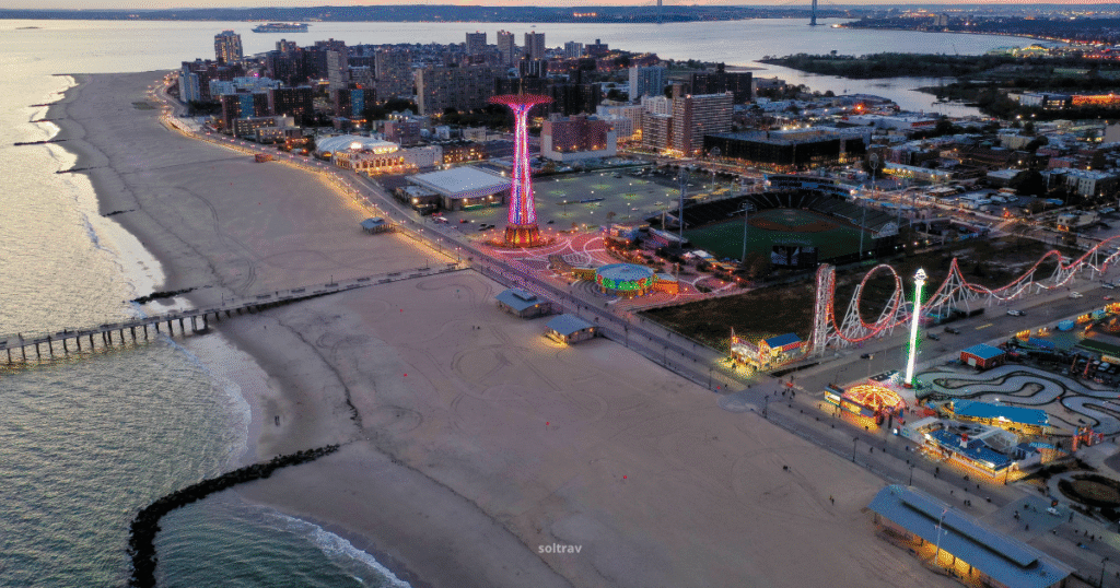 Aerial view of Coney Island's Luna Park at dusk, featuring amusement rides and the beach.