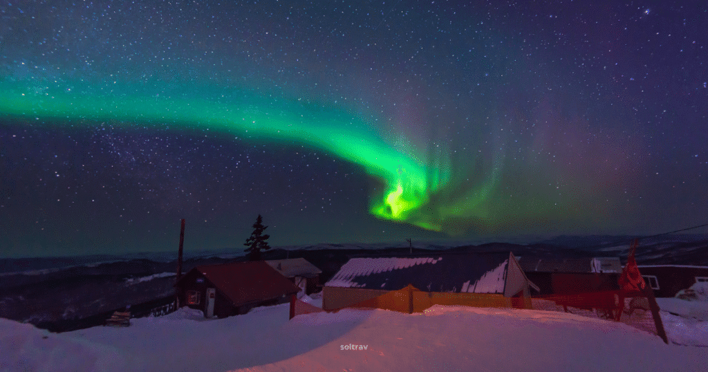 Vibrant Northern Lights over Fairbanks, Alaska, with a starry sky and silhouetted rooftops in the foreground.
