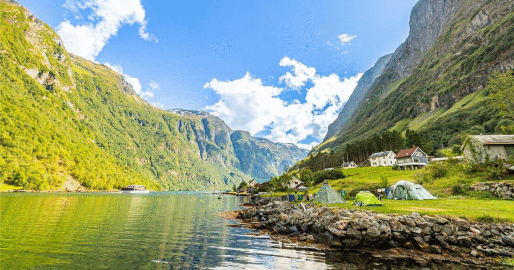 Tents pitched on grassy land beside a peaceful fjord, surrounded by towering green cliffs in Sognefjord, Norway.