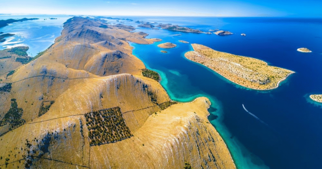 Aerial view of the Kornati Islands in Croatia, showcasing a chain of arid islands surrounded by clear, turquoise waters under a clear blue sky.