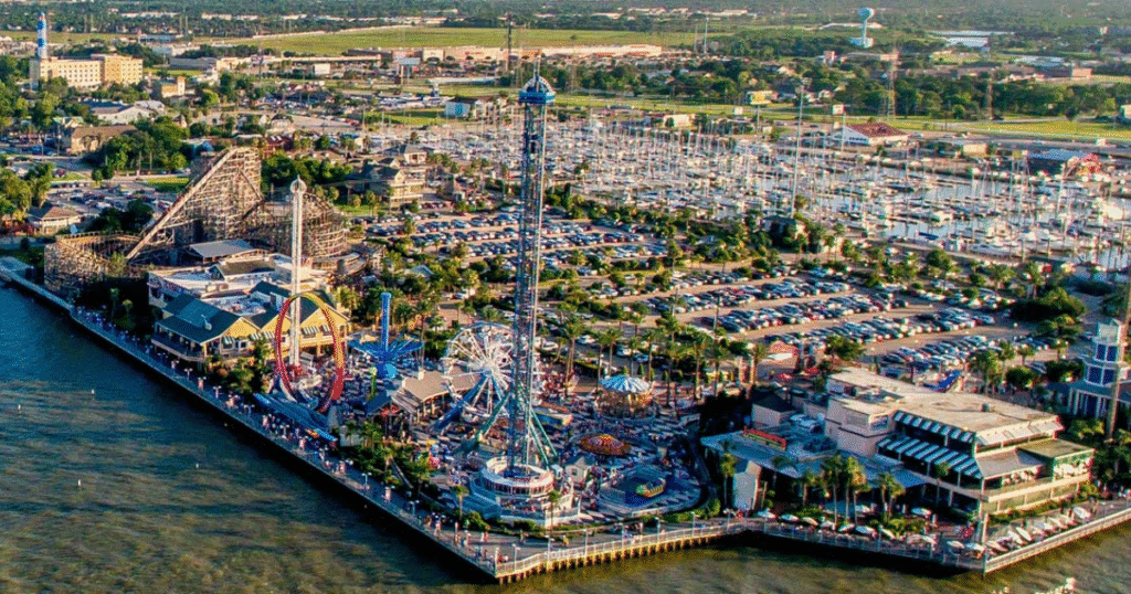 Aerial view of Kemah Boardwalk in Texas, featuring amusement rides, a marina, and a bustling parking area.