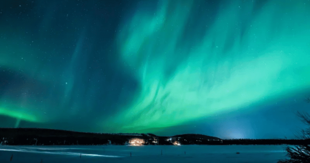 Vibrant Northern Lights illuminate the sky over Kiruna, Sweden, with a snowy landscape and distant lights in the background.