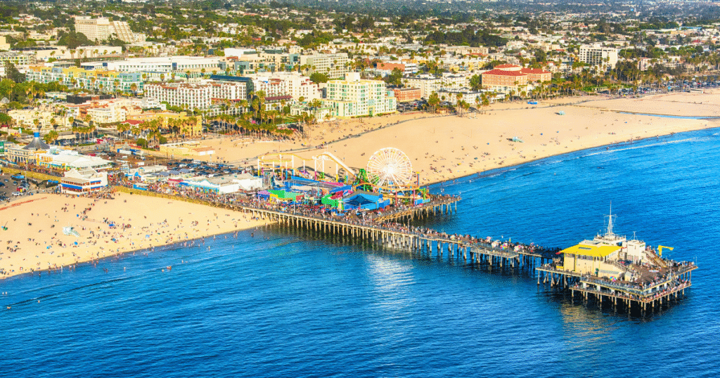 Aerial view of Pacific Park on Santa Monica Pier, showcasing colorful attractions, sandy beaches, and the ocean.
